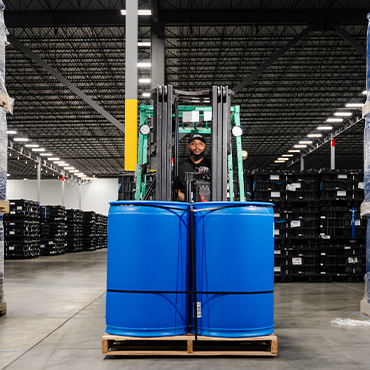 man in black polo and black hat on a forklift facing forward with barrels on a pallet