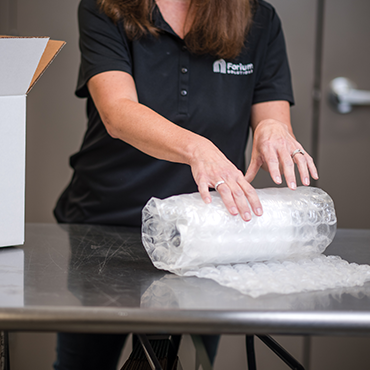woman wrapping a product in bubble wrap on a table next to a cardboard box
