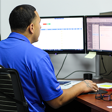 man in blue polo shirt sitting in front of a computer monitor